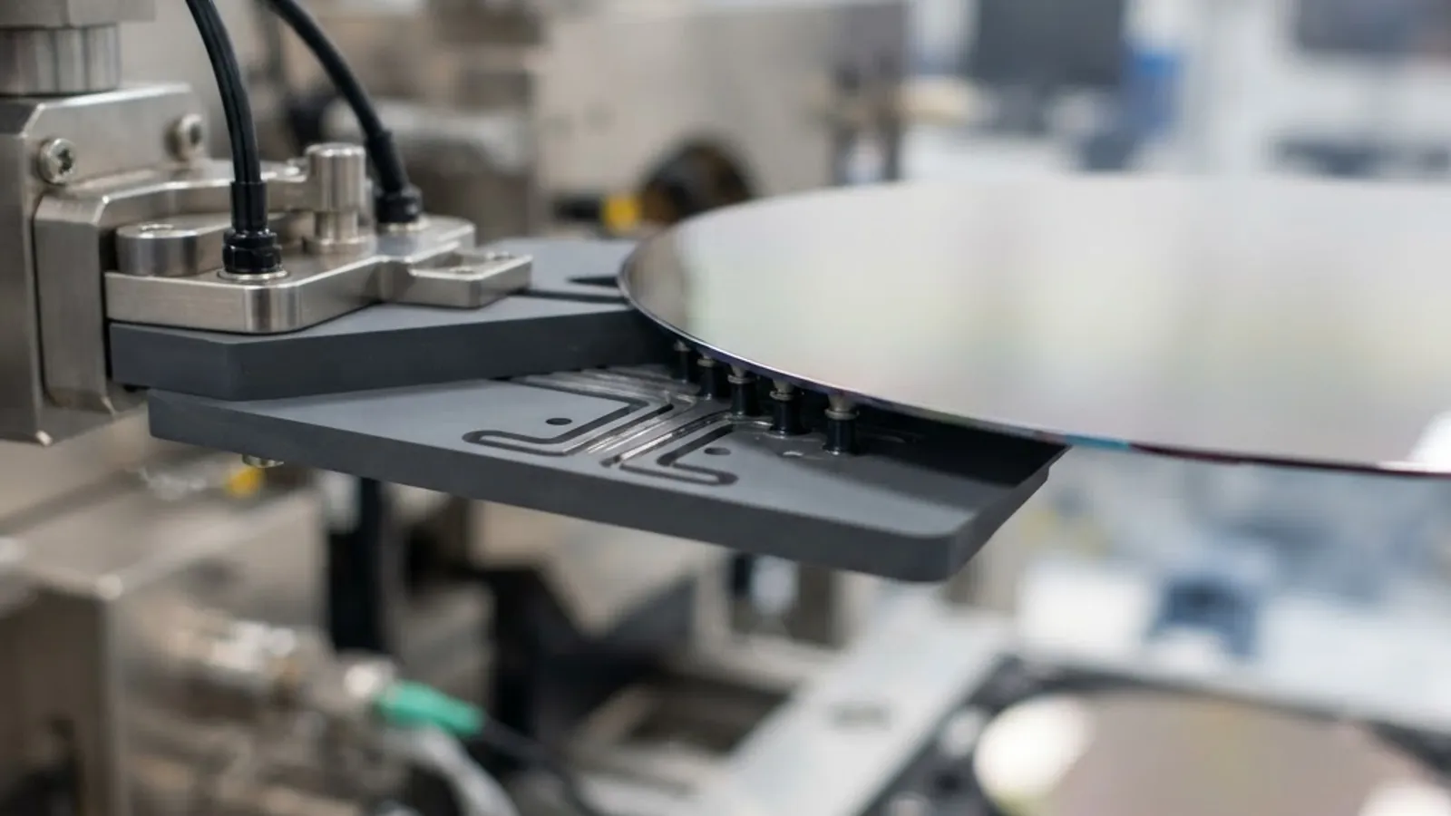 Close-up of a vacuum wafer robot end effector with suction ports gripping a polished silicon wafer